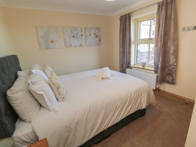 A bedroom with a bed with white bedding and pillows next to a window with curtains at Nook Cottage in Embleton