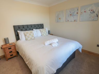 A bedroom with a double bed with white bedding two bedside tables with lamps and three floral paintings on the wall at Nook Cottage in Embleton