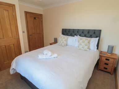 A bedroom with a bed with white bedding and floral pillows beside wooden doors and bedside tables with lamps at Nook Cottage in Embleton