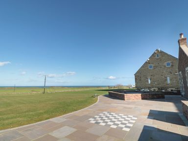 A patio with a built in chessboard on the ground next to a grass field and stone houses at Nook Cottage in Embleton