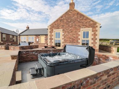 An outdoor area with a hot tub sunken into a brick enclosure and a brick building with windows and a picnic table at Byre Cottage in Embleton