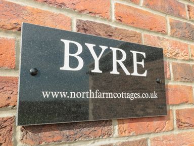 A black rectangular sign with the word BYRE and a website address mounted on a brick wall