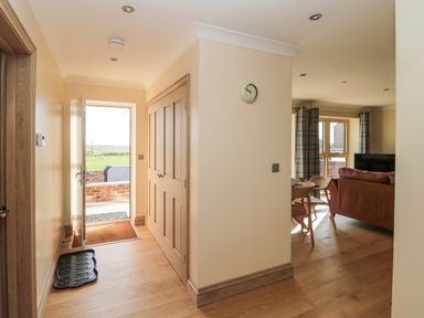 A hallway with wooden floor and doors leading outside and to a living room at Byre Cottage in Embleton