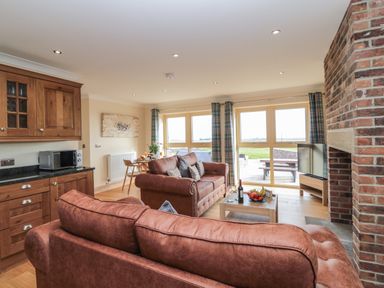 A living room with brown sofas a coffee table with fruit a dining table wooden cabinets and a brick fireplace at Byre Cottage in Embleton