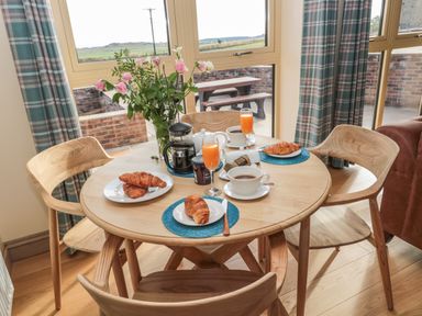 A dining table set with croissants coffee and orange juice next to a window with a view at Byre Cottage in Embleton