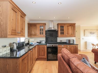 A kitchen with wooden cabinets black countertops oven kettle toaster and a brown sofa at Byre Cottage in Embleton