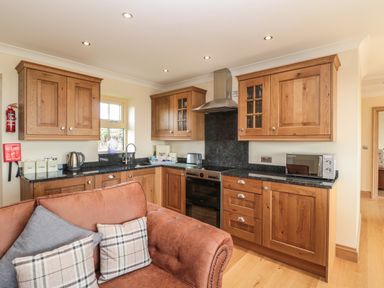 A kitchen with wooden cabinets black countertop and a brown sofa with pillows at Byre Cottage in Embleton