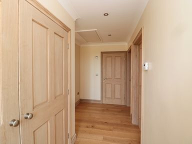 A hallway with wooden doors wooden floor and beige walls at Byre Cottage in Embleton