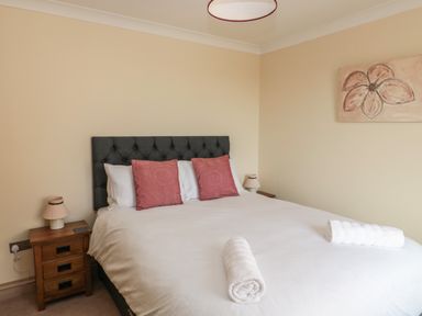 A bedroom with a double bed with white bedding and two red pillows with bedside tables and lamps at Byre Cottage in Embleton