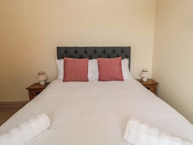 A bedroom with a bed with white linens and two red pillows two bedside tables with lamps