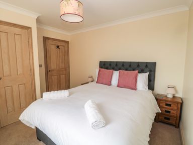 A bedroom with a bed with white bedding and pink pillows two wooden doors and wooden bedside tables with lamps at Byre Cottage in Embleton
