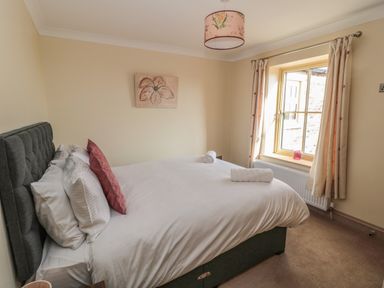 A bedroom with a double bed with white bedding and pillows near a window with curtains at Byre Cottage in Embleton