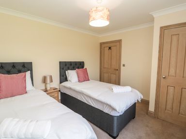 A bedroom with two single beds side by side with white bedding pink pillows and a nightstand with a lamp between the beds at Byre Cottage in Embleton