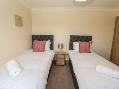 A bedroom with two single beds each with white bedding pillows and a rolled towel with a bedside table with a lamp in between at Byre Cottage in Embleton
