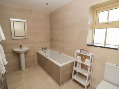 A bathroom with a bathtub sink toilet and a shelving unit near a window at Byre Cottage in Embleton