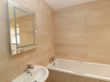 A bathroom with a sink, a mirror, and a bathtub with beige tiled walls at Byre Cottage in Embleton