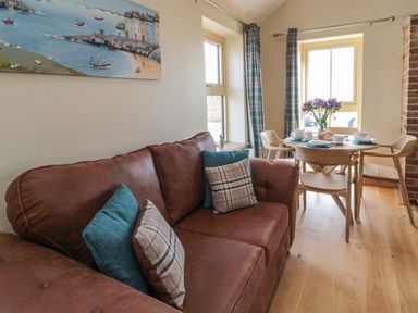A living area with a brown sofa and plaid cushions next to a wooden dining table set with cups and a teapot at Smithy Cottage in Embleton