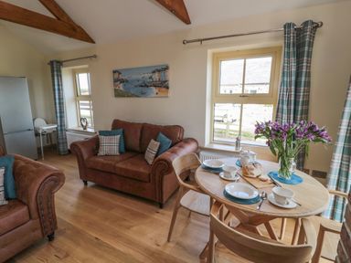 A living room with brown sofas a wooden dining table set with dishes flowers and bread at Smithy Cottage in Embleton