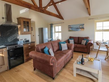 An open living room and kitchen with two brown sofas wooden beams and a coffee table with snacks and drinks at Smithy Cottage in Embleton