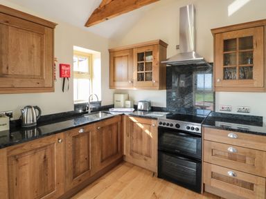 A kitchen with wooden cabinets black countertops a stove and an extractor fan at Smithy Cottage in Embleton