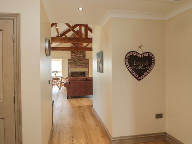 A hallway with wooden floor leading to a living room with a sofa and brick fireplace at Smithy Cottage in Embleton