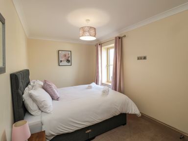 A bedroom with a double bed white bedding and pink pillows next to a window with pink curtains at Smithy Cottage in Embleton