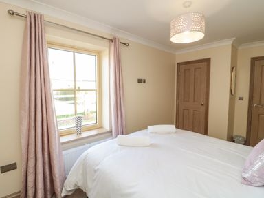 A bedroom with a bed with white linens and towels near a window with pink curtains at Smithy Cottage in Embleton