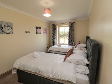 A bedroom with two single beds white bedding and pillows with a window and patterned curtains at Smithy Cottage in Embleton