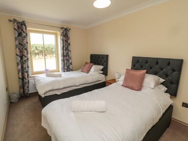A bedroom with two single beds a window with patterned curtains and a small bedside table at Smithy Cottage in Embleton