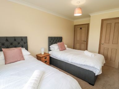 A bedroom with two single beds with pink cushions and rolled towels a wooden bedside table and doors at Smithy Cottage in Embleton