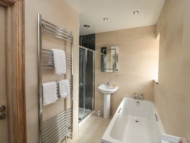 A bathroom with a bathtub sink shower and towel rack at Smithy Cottage in Embleton