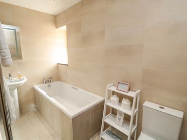 A bathroom with a bathtub sink toilet and a white shelf with toiletries at Smithy Cottage in Embleton