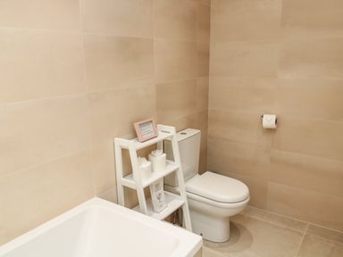 A bathroom with a white toilet a small white shelving unit beside it and a bathtub at Smithy Cottage in Embleton