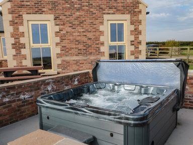 An outdoor hot tub with bubbling water next to a brick wall and a picnic table outside a brick house