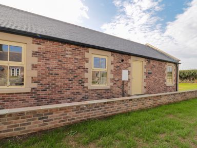Exterior of a brick house with three windows a door and a low brick wall in front at Smithy Cottage in Embleton