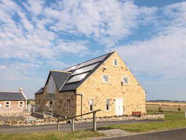 A stone house with solar panels on the roof and surrounding fields at Smithy Cottage in Embleton