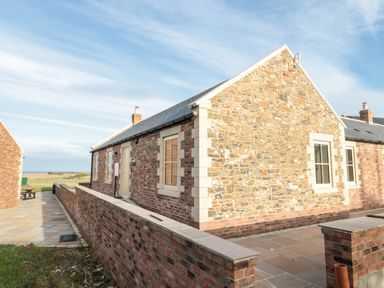 Exterior view of a stone and brick cottage with paved walkway and low brick wall at Bothy Cottage in Embleton