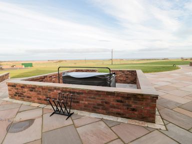 An outdoor area with a covered hot tub surrounded by low brick walls and a lawn in the background at Bothy Cottage in Embleton
