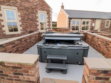 An outdoor hot tub with steps surrounded by brick walls between brick buildings at Bothy Cottage in Embleton