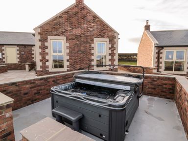 An outdoor hot tub on a patio surrounded by brick walls with brick houses in the background at Bothy Cottage in Embleton