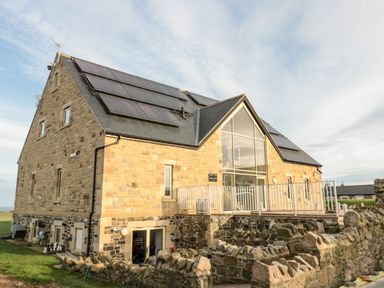 A stone building with solar panels on the roof and a glass front at Bothy Cottage in Embleton