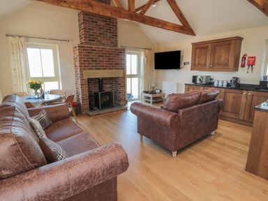 A living room with brown leather sofas a brick fireplace a dining table and wooden kitchen cabinets at Bothy Cottage in Embleton