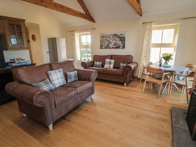 A living room with two brown sofas with cushions and a dining table with chairs and flowers at Bothy Cottage in Embleton