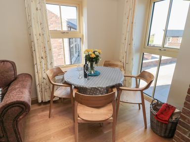 A dining table with four wooden chairs near windows and a basket with a red cloth at Bothy Cottage in Embleton