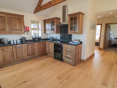 A kitchen with wooden cabinets black countertops and wooden floor at Bothy Cottage in Embleton
