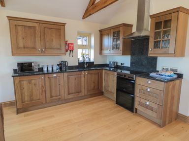A kitchen with wooden cabinets black countertops a stove microwave kettle and toaster at Bothy Cottage in Embleton