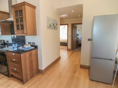 A kitchen area with wooden cabinets a countertop refrigerator and a hallway leading to bedrooms at Bothy Cottage Embleton