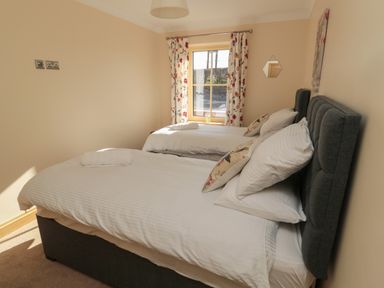 A bedroom with two single beds with white bedding and floral curtains at Bothy Cottage in Embleton