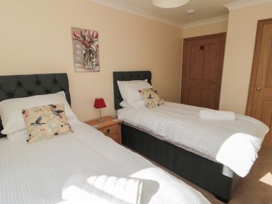 A bedroom with two single beds a wooden nightstand with a lamp and a floral painting on the wall at Bothy Cottage in Embleton