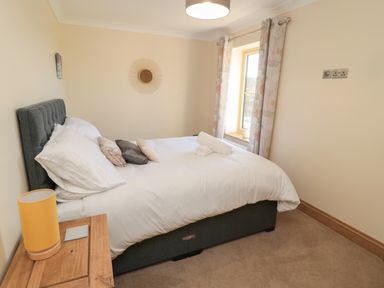A bedroom with a bed with pillows and rolled towels a wooden side table with a lamp and a window with curtains at Bothy Cottage in Embleton